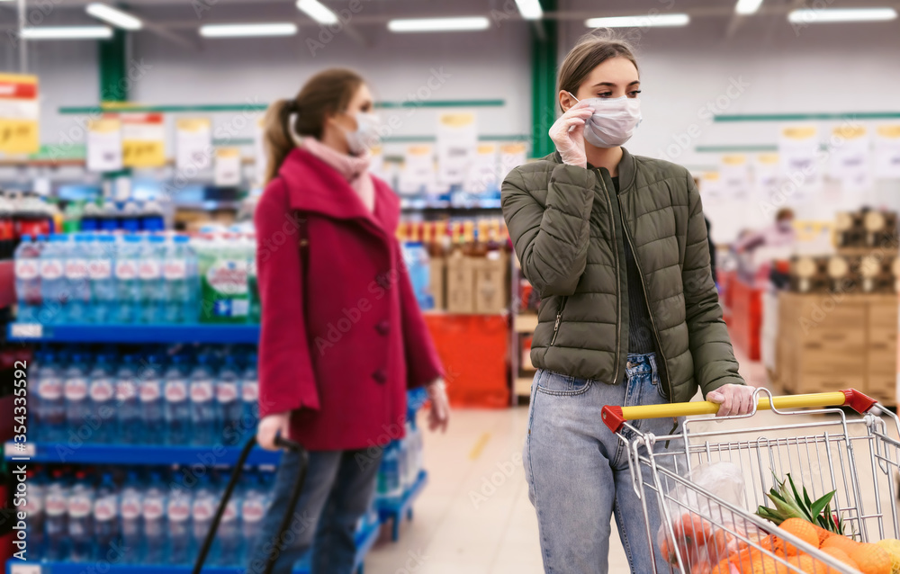 Social distancing in a supermarket. A young women in a disposable face masks and gloves with grocery basket. Shopping during the Coronavirus Covid-19 epidemic 2020
