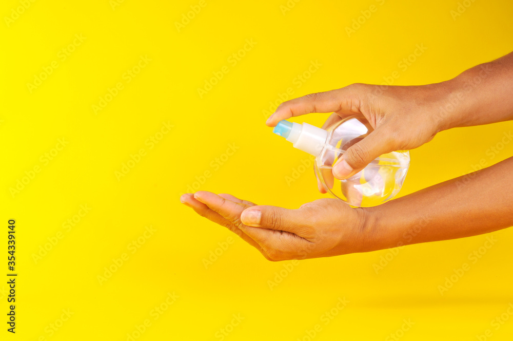 Hand of man applying alcohol spray or anti bacteria spray to prevent spread of virus and bacteria. Applying alcohol spray on hand isolated on yellow background. Hand of man applying alcohol spray or anti bacteria spray to prevent spread of virus and bacteria. Applying alcohol spray on hand isolated on yellow background.