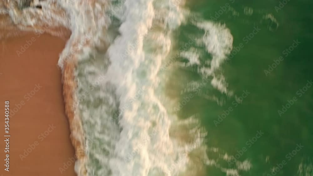 Aerial top view of ocean blue waves break on a beach. Sea waves and beautiful sand beach aerial view drone shot. Bird's eye view of ocean waves crashing against an empty sand beach from above. Aerial top view of ocean blue waves break on a beach. Sea waves and beautiful sand beach aerial view drone shot. Bird's eye view of ocean waves crashing against an empty sand beach from above.
