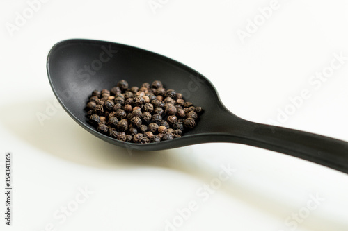 Black peppercorns on a big black plastic spoon. White background. 