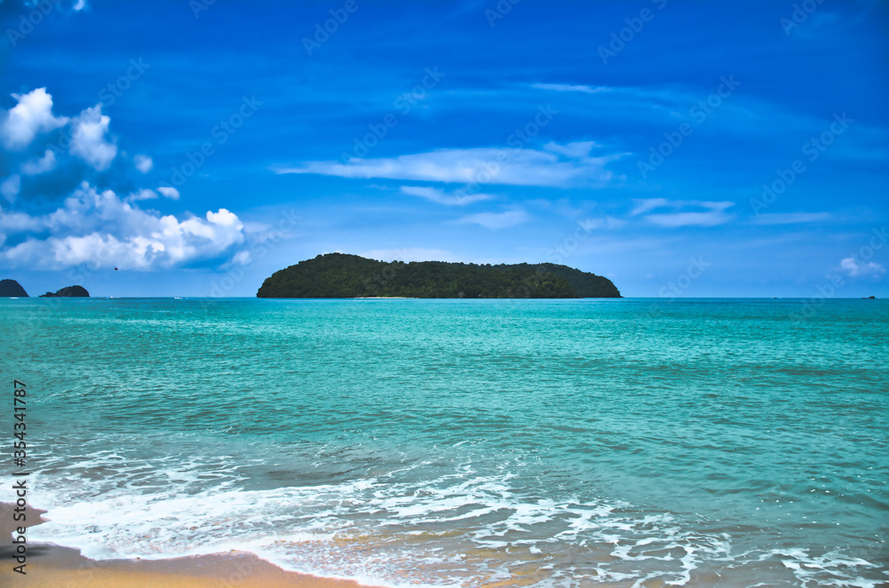 Waves of the azure Andaman sea under the blue sky reaching the shores of the sandy beautiful exotic and stunning Cenang beach in Langkawi island