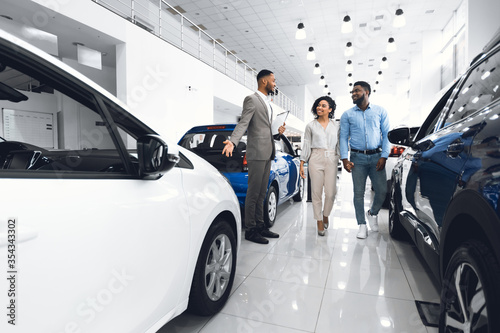 Cheerful Manager Showing Automobile To Customers In Dealership Store