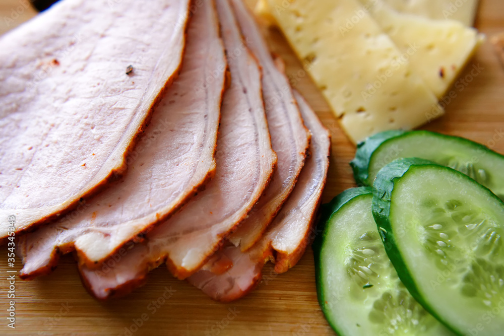 Slicing ham, cucumbers and cheese with ruddy thin breads lie on a wooden board. Slicing ham, cucumbers and cheese with ruddy thin breads lie on a wooden board.