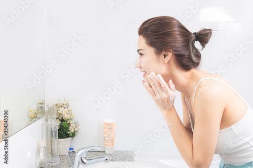 Asian woman wash her face in the bathroom before shower.