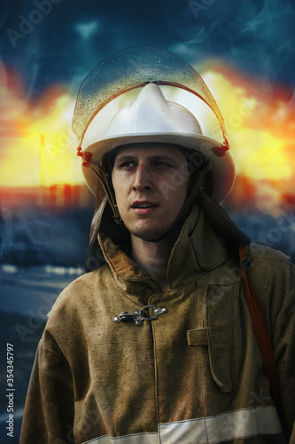 Portrait of a firefighter in a helmet and special clothes against the background of the fire. A young rescuer of Caucasian nationality © SerPak