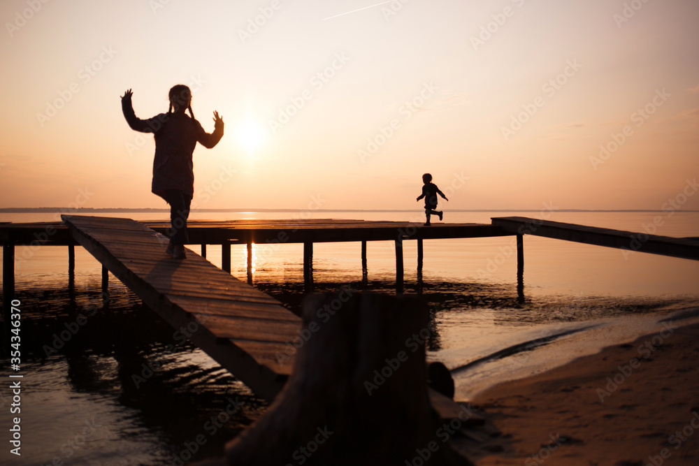 Fototapeta premium silhouettes of people children on shore lake. Summer sunset on water. evening walk outdoor on bridge