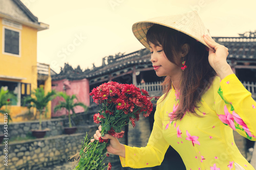 Selective focus on red flowers, beautiful women in Ao Dai Vietnam traditional dress holidng a branch of red flowers