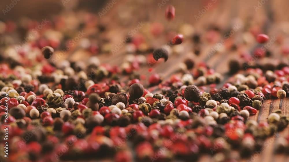 Mixed peppercorns falling on wooden table, heap of spice, mix of different peppers closeup, 240 fps slow motion