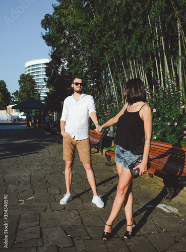 Happy couple of lovers walking outdoors. Bamboo gardens at background. Cheerful, smiling man and lucky woman in sunglasses have fun time in summer. © Khrystyna Bohush