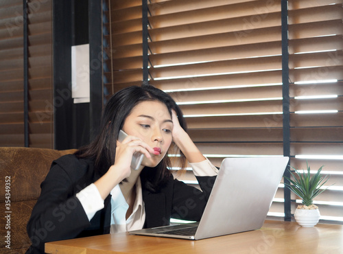 Asian businesswoman in suit talking on mobile phone in modern office.Stressed businesswoman working on computer.Global recession on covid19.