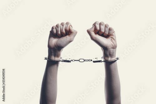 two hands on a white background with fingers gathered towards fists with handcuffs on hands