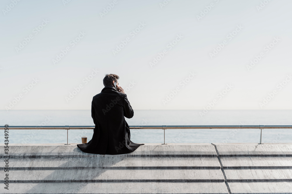 Businessman sitting on quay wall talking on cell phone Businessman sitting on quay wall talking on cell phone