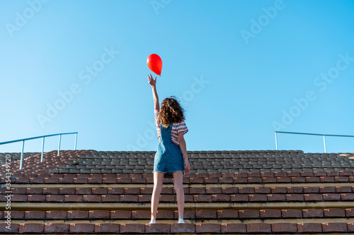 Young woman standing on granstand, letting go of a red ballon