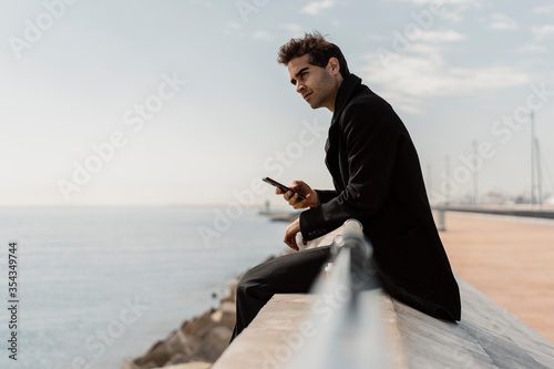 Businessman sitting on quay wall with cell phone photo