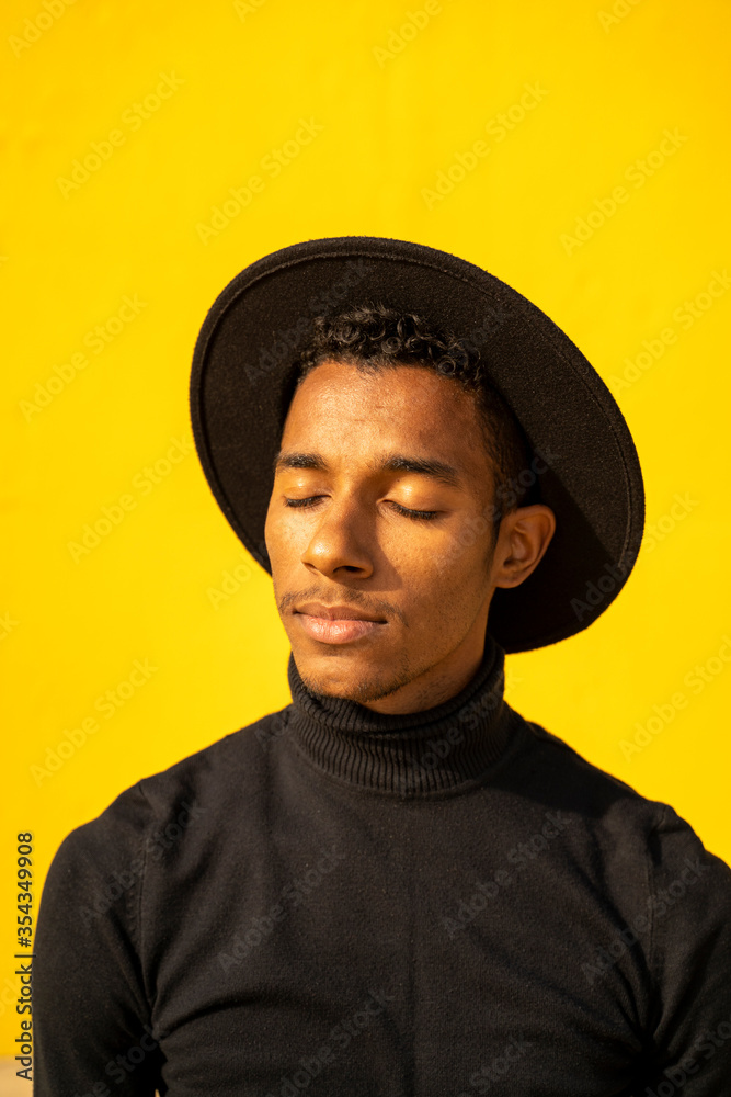 Portrait of young man, wearing black in front of yellow wall, eyes closed