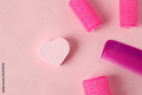 The concept of love for the chosen business-hairdressing services: heart on a pink background with curlers and a comb, top view, place for the inscription