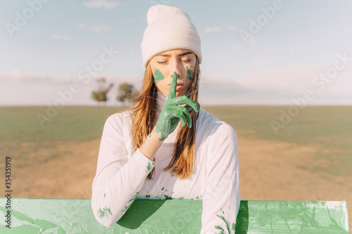 Young woman putting finger of green hand on her mouth