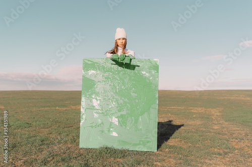 Young woman holding green painting on dry field photo