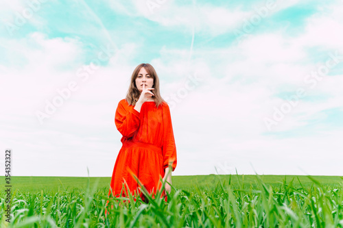 Portrait of woman wearing red dress standing in a field with finger on mouth