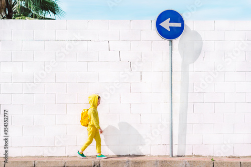 Girl walking at a traffic sign, direction left, in front of a white wall photo