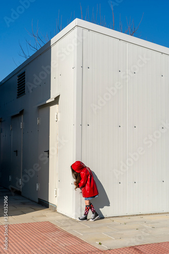 Little girl wearing red rain coat hiding behind a corner