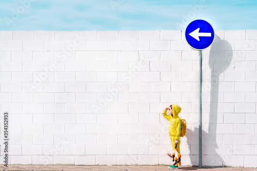 Girl with her cuddly toy at traffic sign, direction left, in front of a white wall