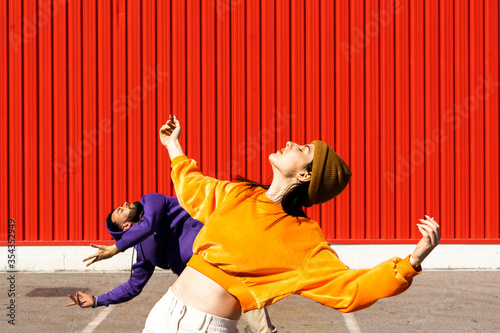 Young man and woman performing on road in front of red wall