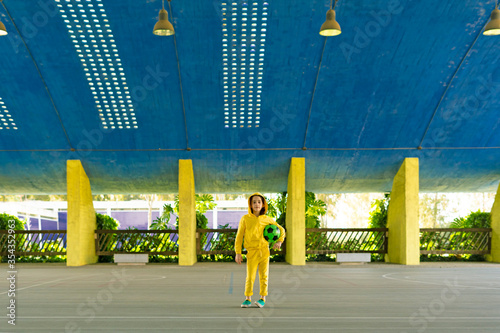 Portrait of girl in yellow tracksuit holding soccer ball outdoors