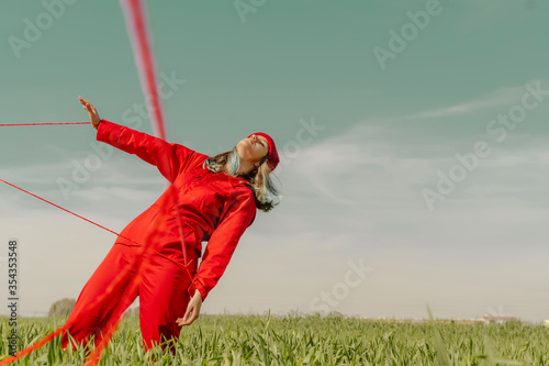 Young woman wearing red overall and hat performing on a field with red string