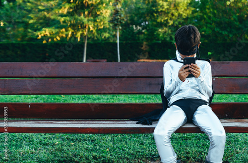 Portrait of boy disguised as superhero using mobile phone on park bench photo