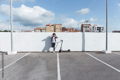 Young man with e-scooter and headphones on parking deck