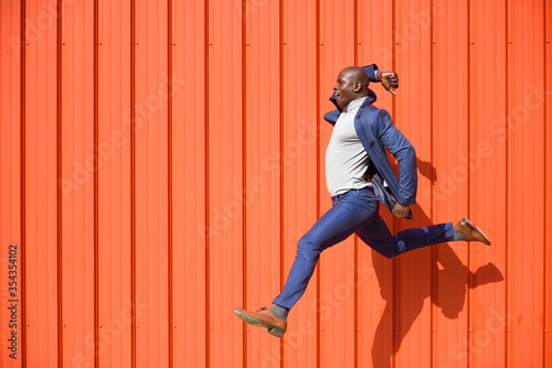 Businessman jumping in the air in front of orange wall photo