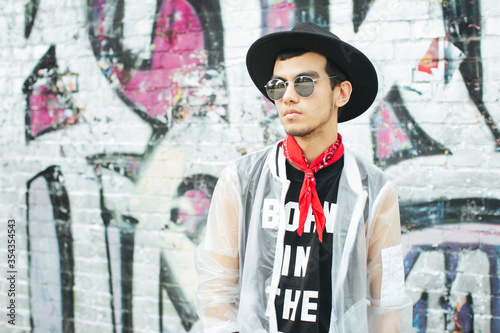 Fashionable young man with hat and sunglasses wearing translucent rainjacket