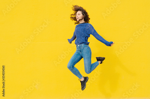 Young woman jumping in the air in front of yellow background