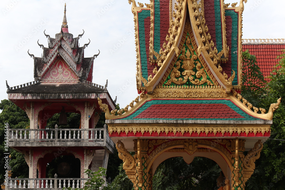 Decorative and colorful roof top of a pavillion and a mulit-level bell tower in the back at a temple site in Siamese Lao PDR, Southeast Asia