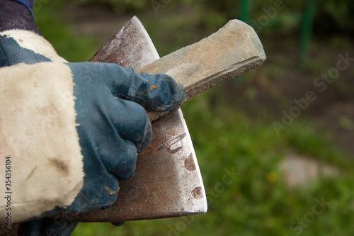 A man in gloves sharpens an iron axe with a special knife stone. A place for inscription. photo