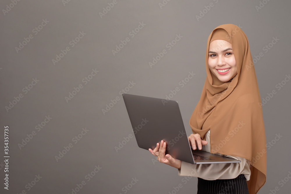 Naklejka premium Portrait of beautiful woman with hijab is holding computer laptop on gray background