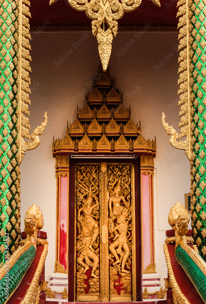Entrance and doorway showing a golden decorated wooden ancient door with various buddha images in Siamese Lao PDR, Southeast Asia