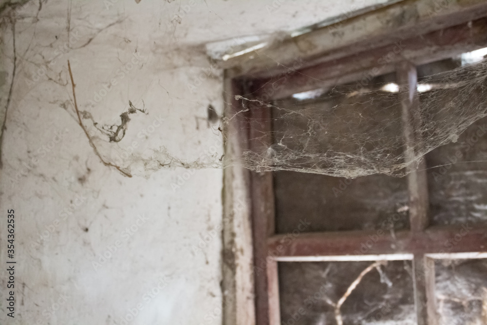 Gloomy window with cobwebs in an abandoned house. Old web on the window and in the corners. Creepy atmosphere, darkness