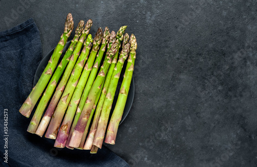
Raw green asparagus in a black plate on a stone background with copy space for your text
