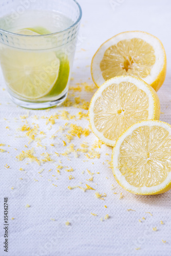 Aerial view of half lemons, zest and glass cup with juice, on white cloth, selective focus, vertical