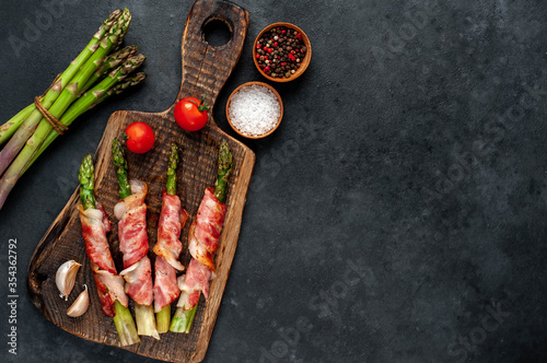  Baked asparagus with bacon and spices on a cutting board on a stone background with copy space for your text
