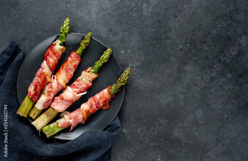  Baked asparagus with bacon and spices on a black plate on a stone background with copy space for your text