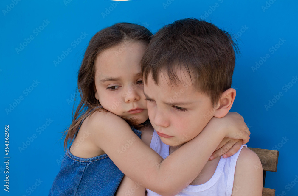Little upset brother and sister. Isolated on a blue background. The concept of family love. Little upset brother and sister. Isolated on a blue background. The concept of family love.