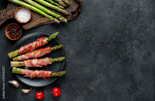  Baked asparagus with bacon and spices on a black plate on a stone background with copy space for your text