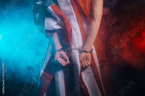 an arrested man from the back with handcuffs on him, the American flag on his back