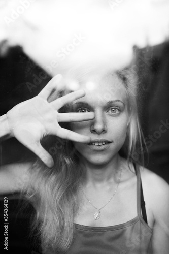 Black and white picture of handsome young girl with fair hair behind glass and covers her face with the hand vand say to stop photo