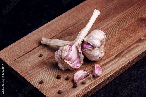 Two heads of garlic and black pepper peas on a wooden board