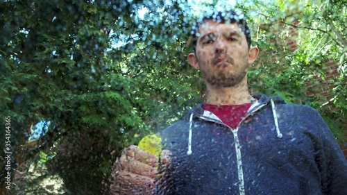 High quality close-up 4k slow motion video of a blurred man wiping wet window glass and holding spray bottle on a bright summer nature background.