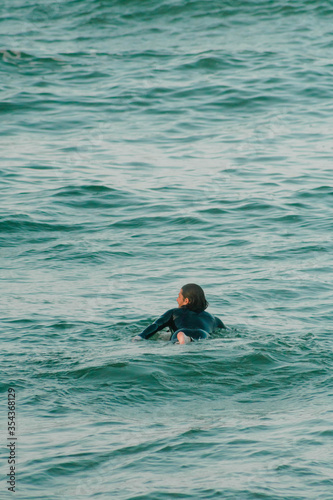 A surfer dressed in wetsuit swimming to the point where the wave breaks